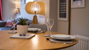 Une table à manger dressée avec des assiettes, des couverts et des verres à vin, avec une plante en pot et une lampe en arrière-plan.