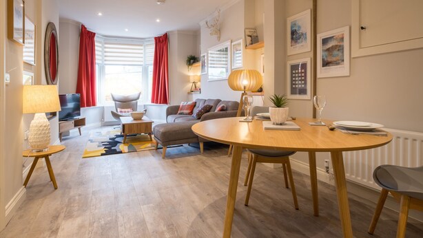 Un salon moderne avec un coin repas, comprenant une table ronde en bois, un ensemble de canapés et un rideau rouge.