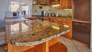 Una cocina con encimeras de granito, armarios de madera, un refrigerador de acero inoxidable y un ventanal con vistas.