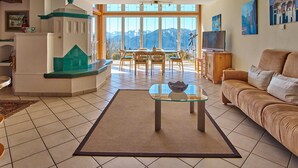 Ein Wohnzimmer mit Glastisch, einer Couch, einem Essbereich mit Stühlen und einem Fernseher auf einer Holzkommode.