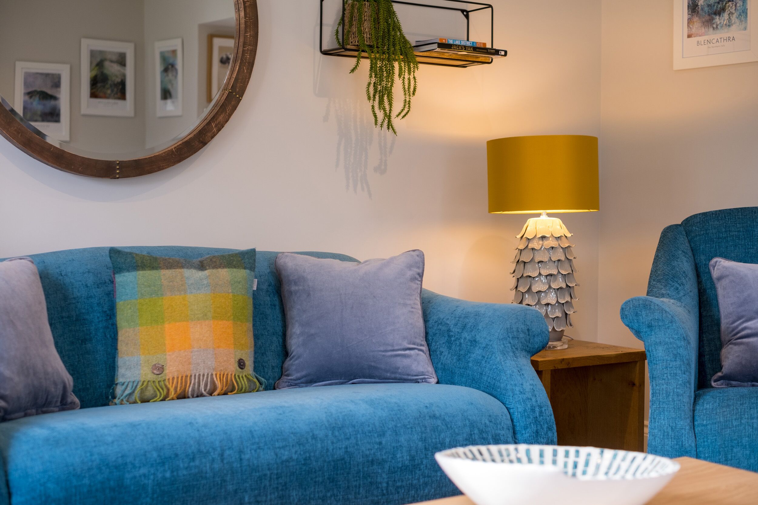 Un canapé bleu avec un plaid à carreaux, une lampe avec un abat-jour doré et un miroir au mur.