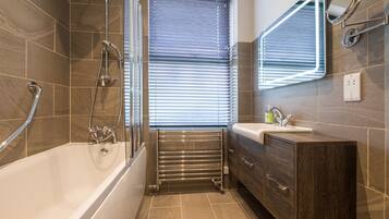A modern bathroom with a bathtub, a vanity with a mirror, and a window with blinds.