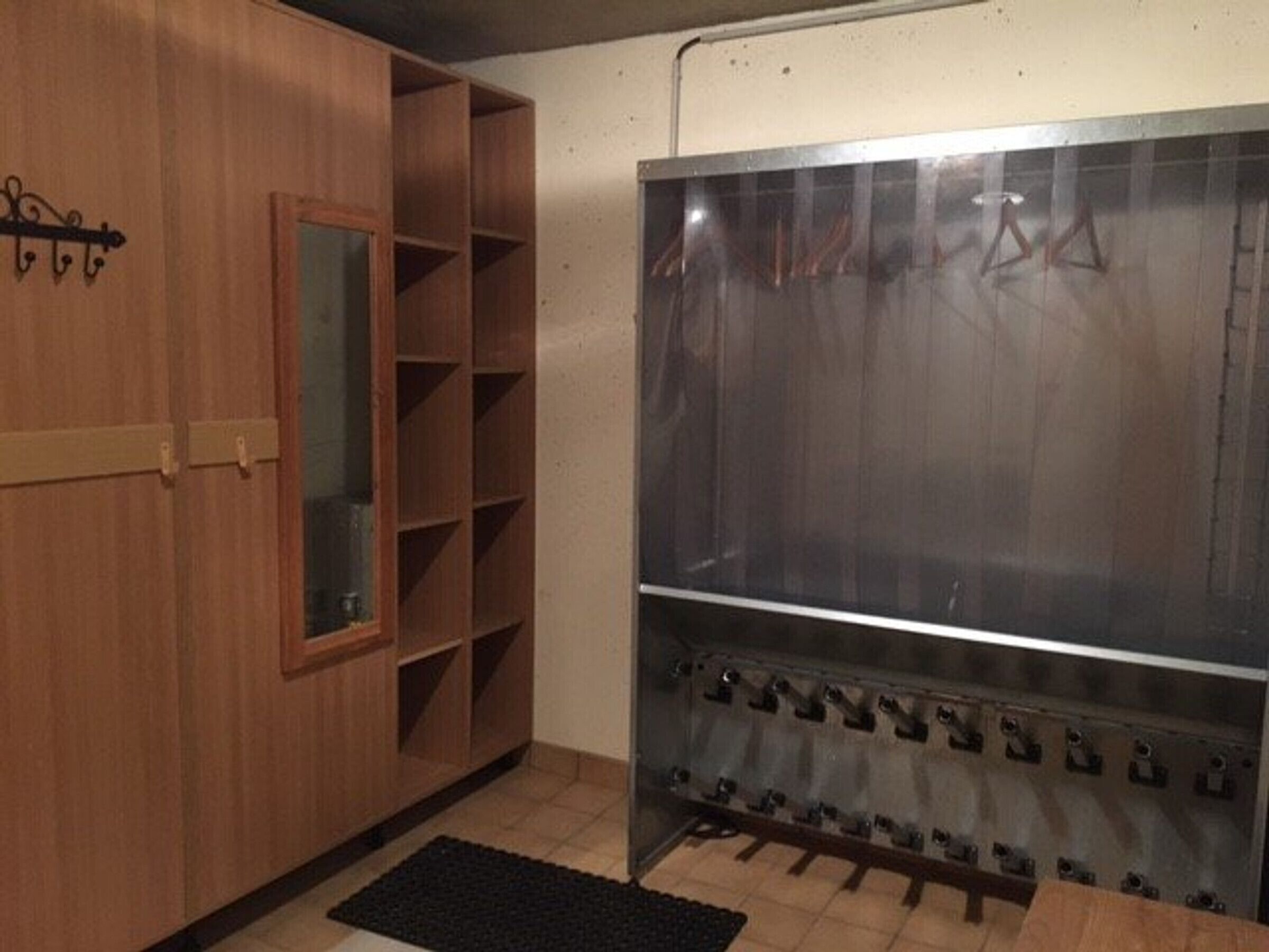 A room with a wooden wardrobe, a mirror, and a large metallic appliance with multiple hooks.