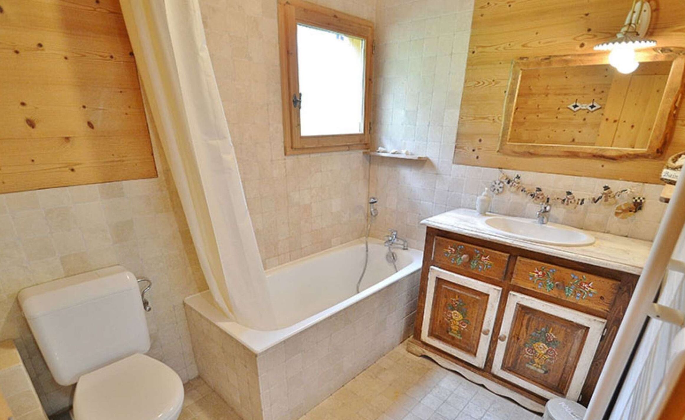 Et badeværelse med trægulv, badekar, toilet og vask med dekorative skabsdøre.