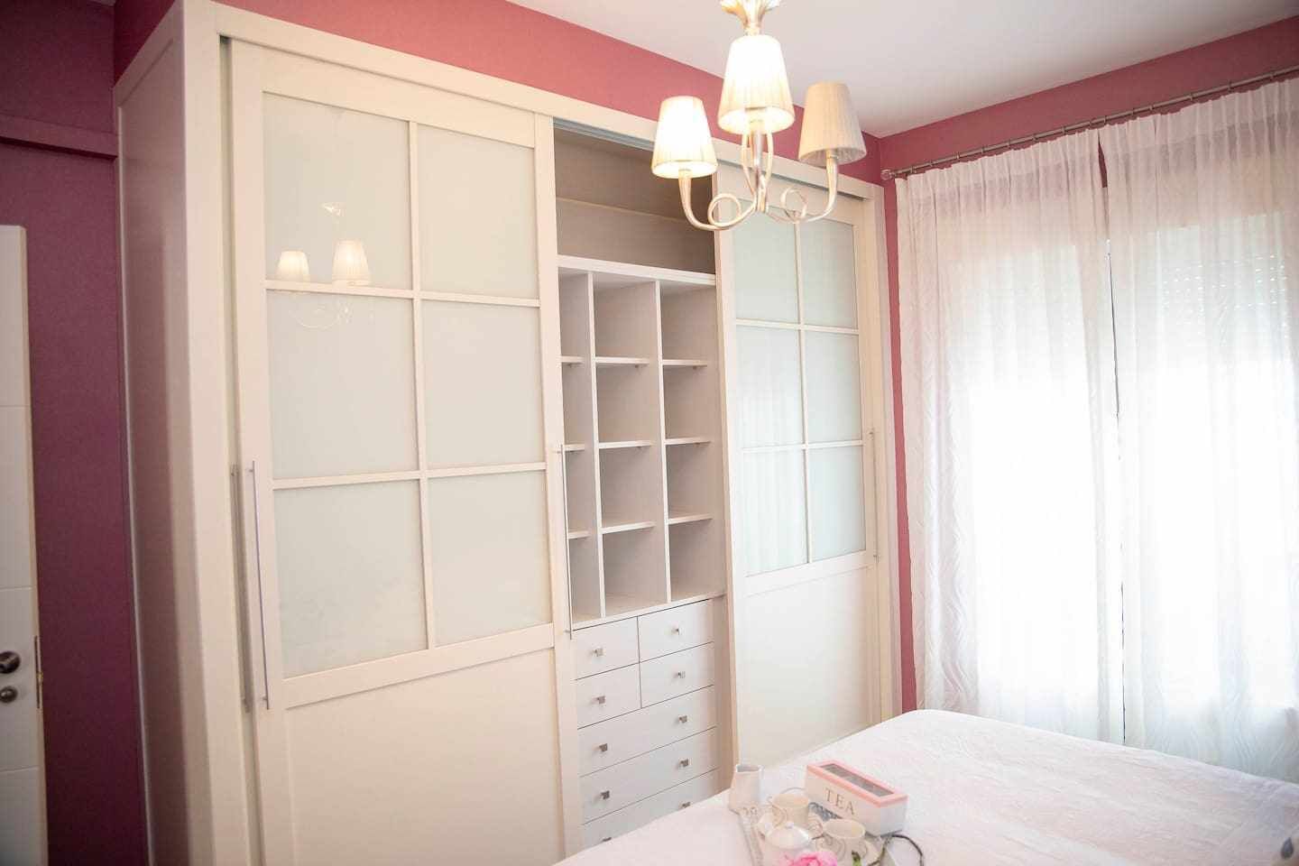 A bedroom with a large wardrobe, a bed, and a chandelier.