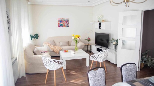 Un salon moderne comprenant un canapé, deux fauteuils blancs, une table basse, un téléviseur et une plante décorative.