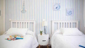 Une chambre avec deux lits, un papier peint à rayures et des œuvres d’art encadrées accrochées au mur.