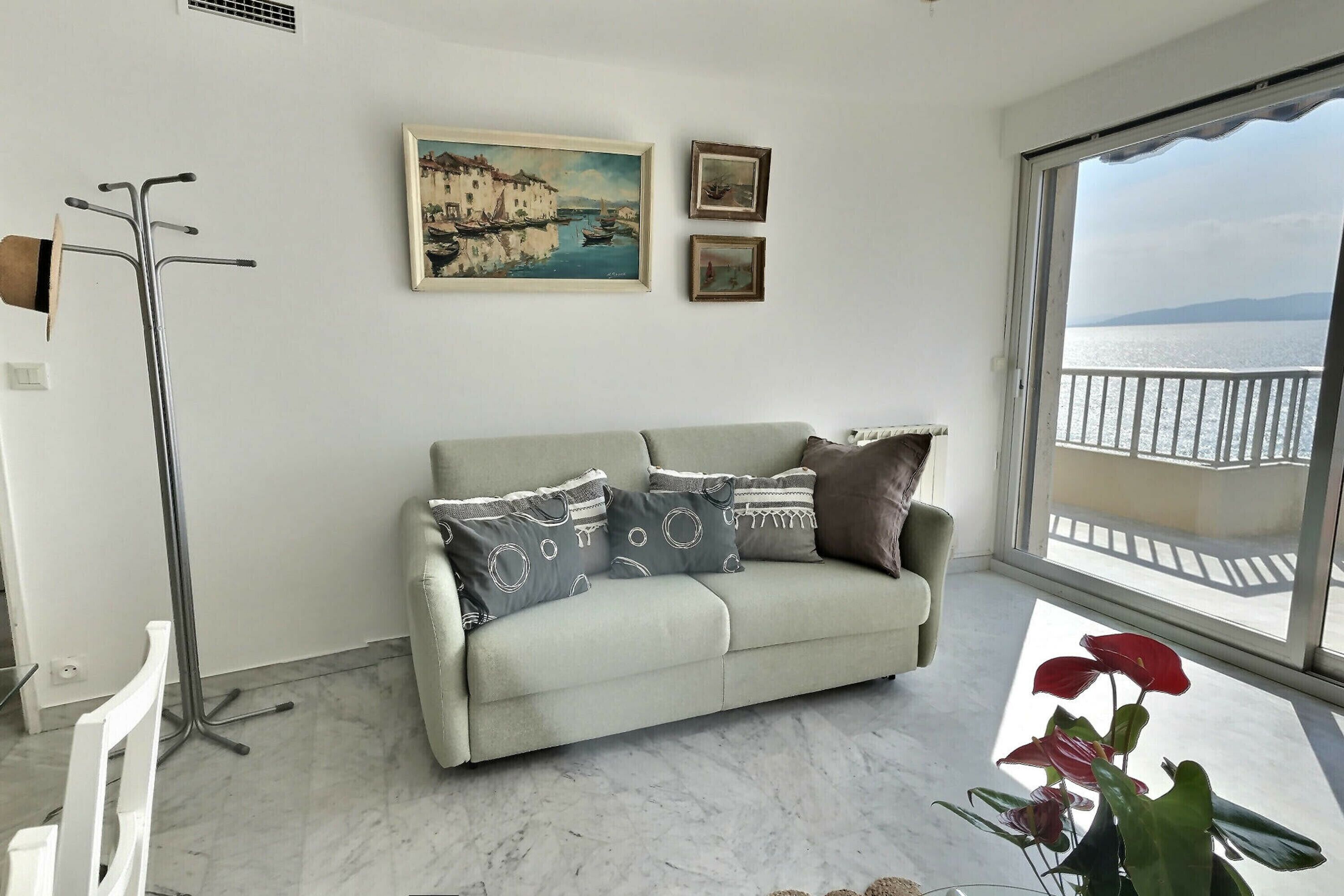 A living room with a sofa, a floor lamp, and a large window with a view of the sea.