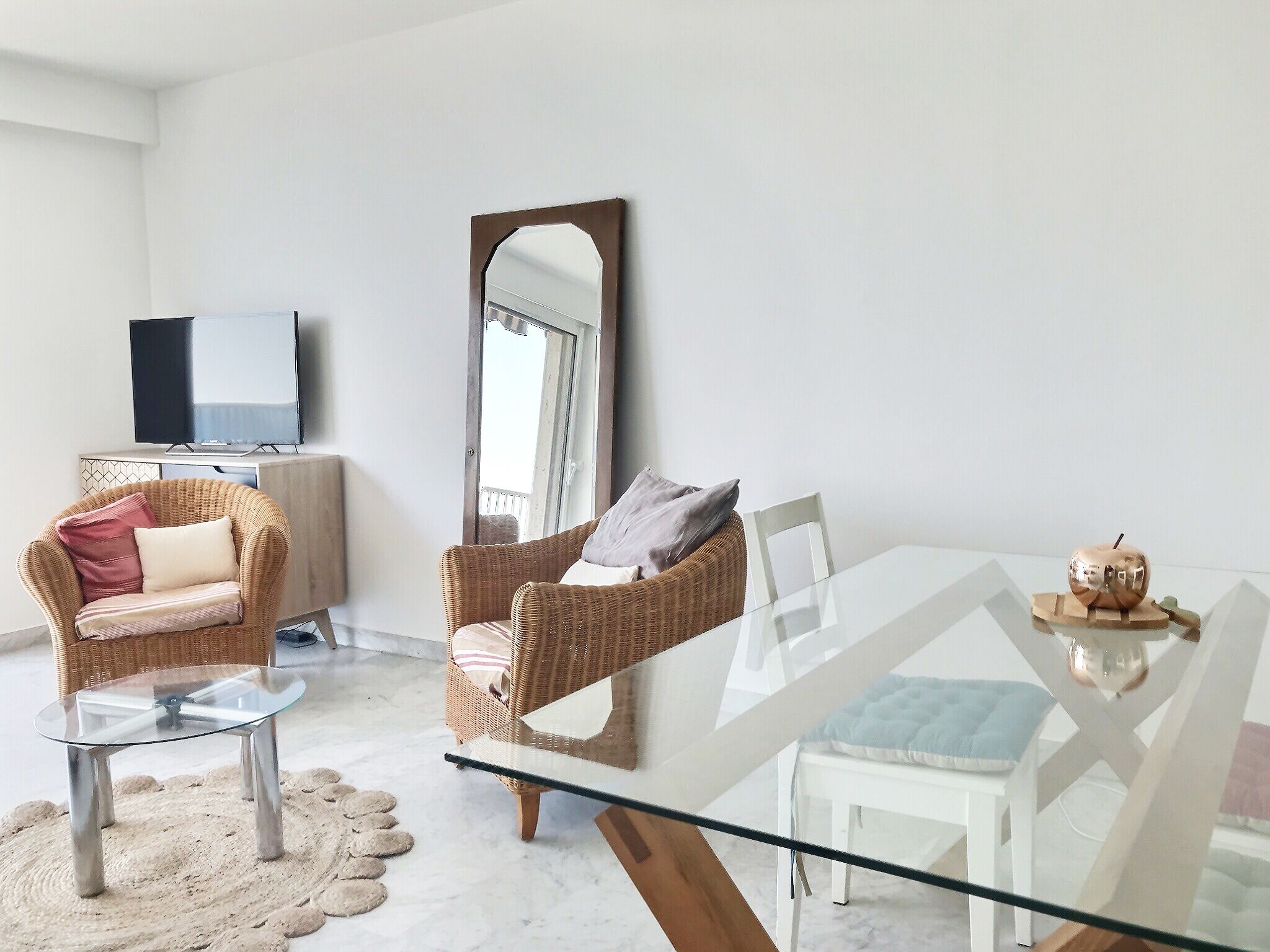 A modern living room with wicker furniture, a glass dining table, and a flat-screen TV.