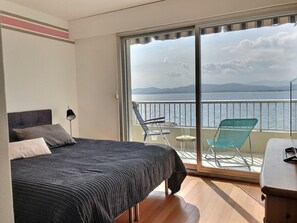 A bedroom with a bed, a nightstand, a lamp, and a view of the sea through a sliding glass door. - Breathtaking views/standing/all on foot (Saint-Raphaël)