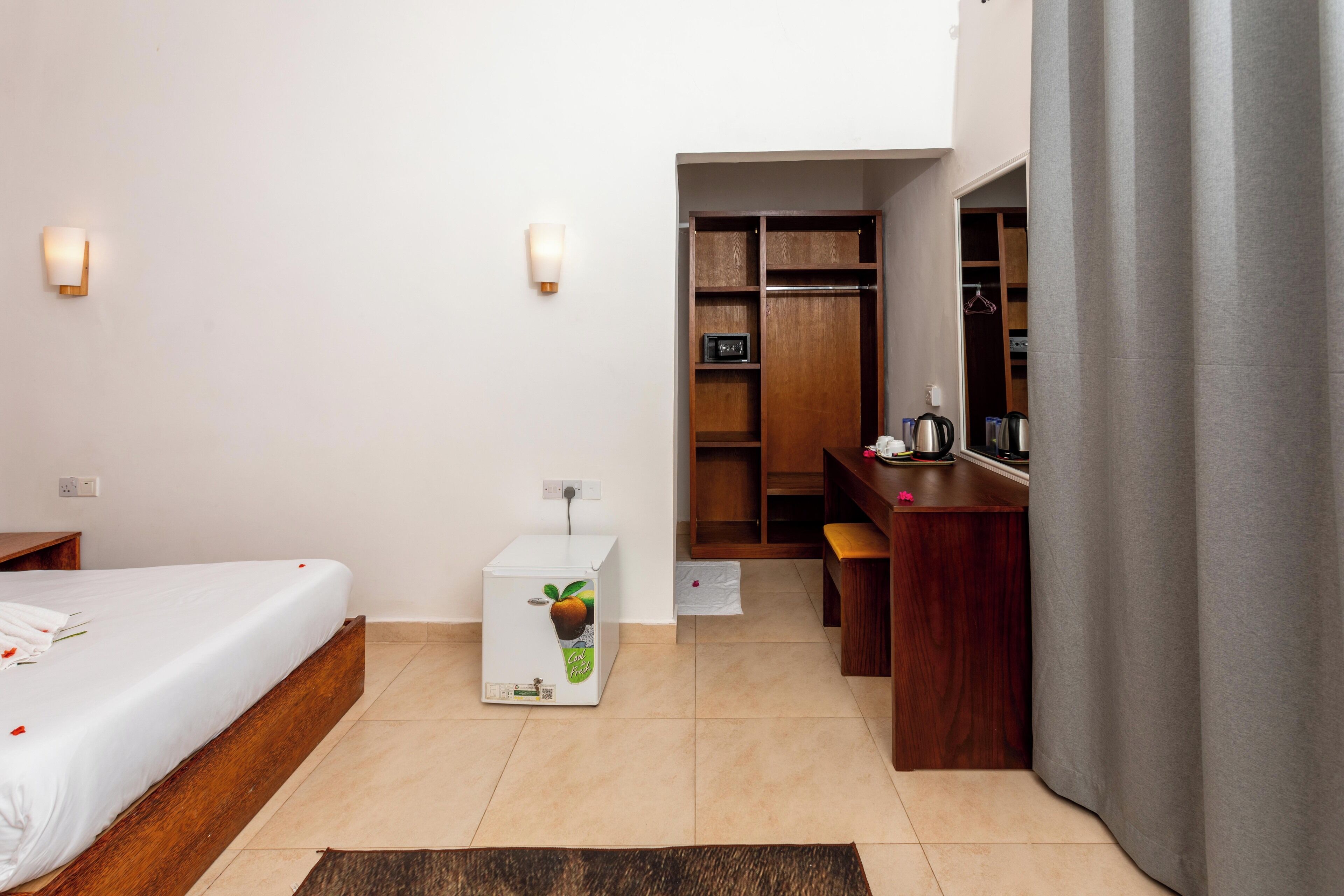 A hotel room with a bed, a small refrigerator, a desk, and a wardrobe.