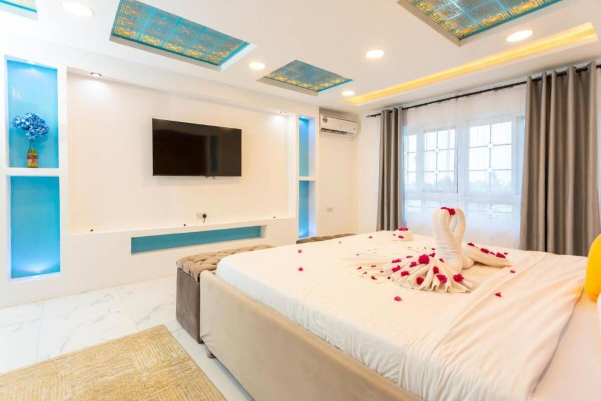 Habitació d'hotel moderna amb un llit gran, una televisió de pantalla plana, un sostre amb panells decoratius i una finestra amb cortines.