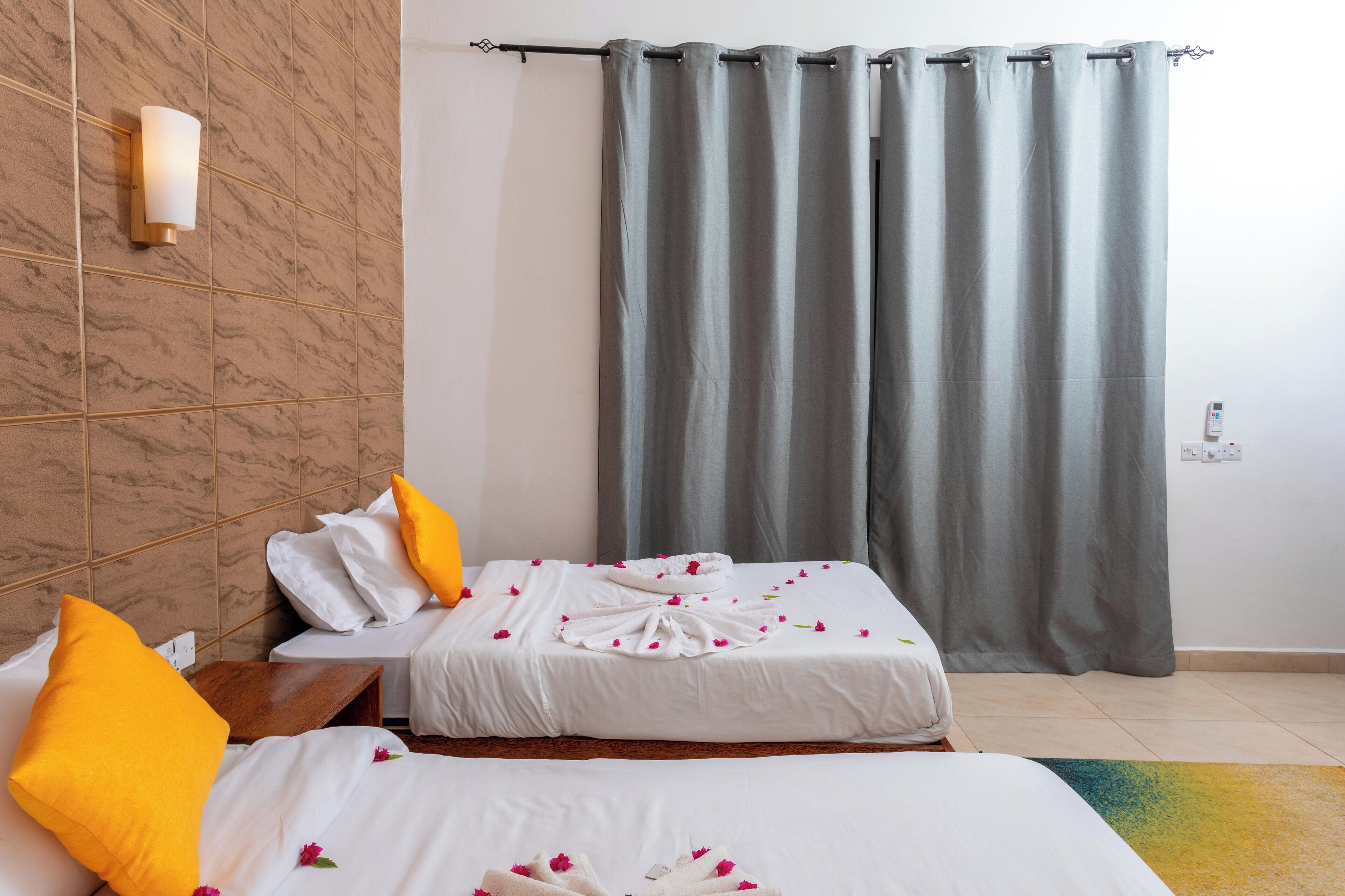 A hotel room with two beds, a marble wall, a grey curtain, and a wall-mounted light fixture.