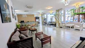Un hall d’entrée spacieux avec un piano, des fauteuils confortables, un comptoir d’accueil et un espace piscine visible à travers les murs de verre.
