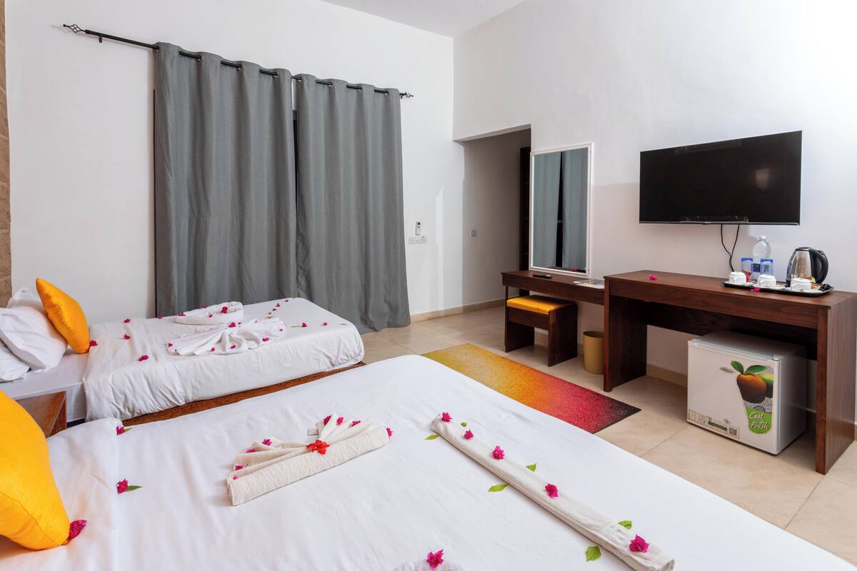 Habitació d'hotel amb dos llits, una taula de treball, televisió i nevera.
