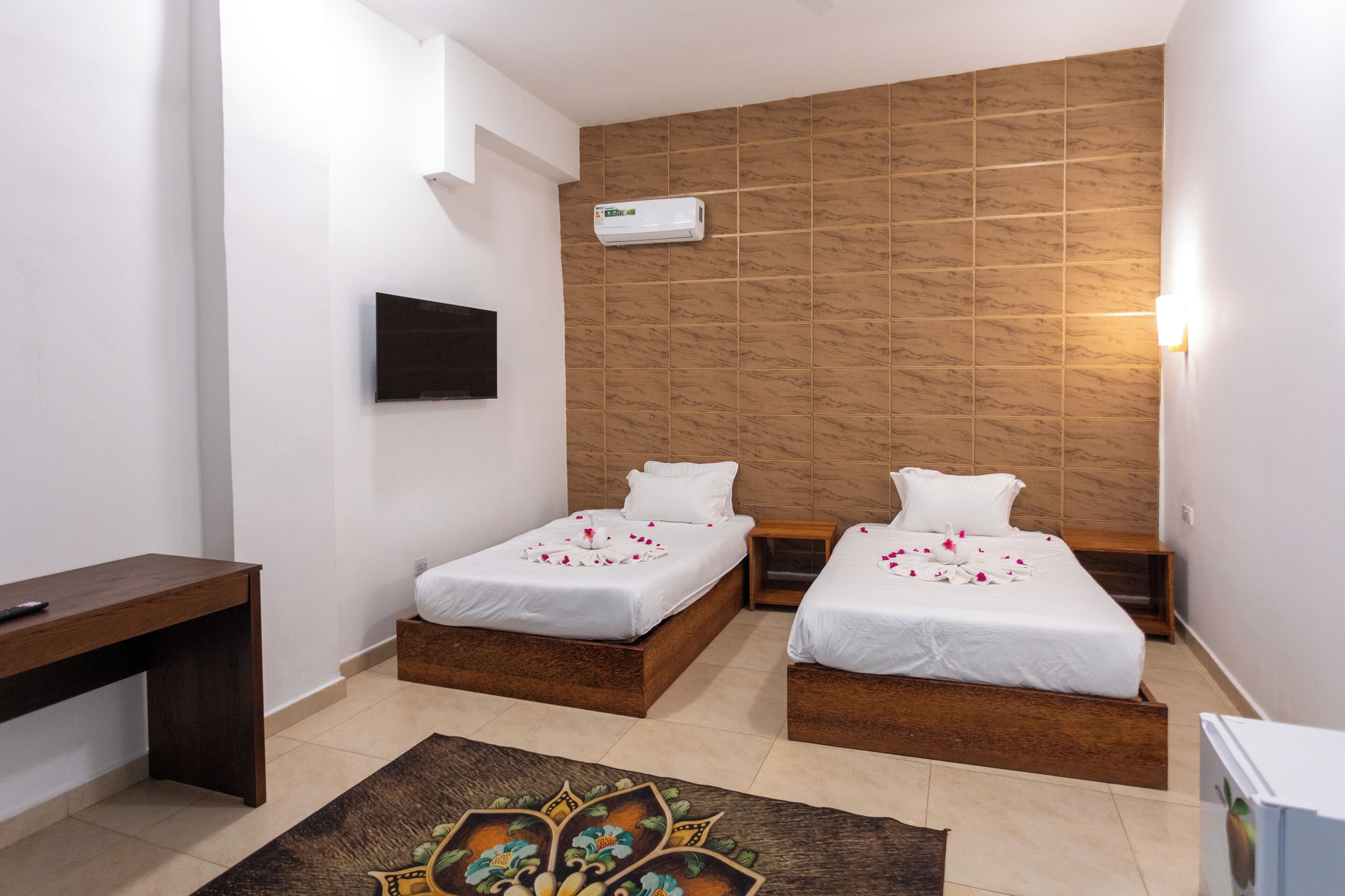 Une chambre d’hôtel avec deux lits simples, un bureau, une télévision et un climatiseur fixé au mur.