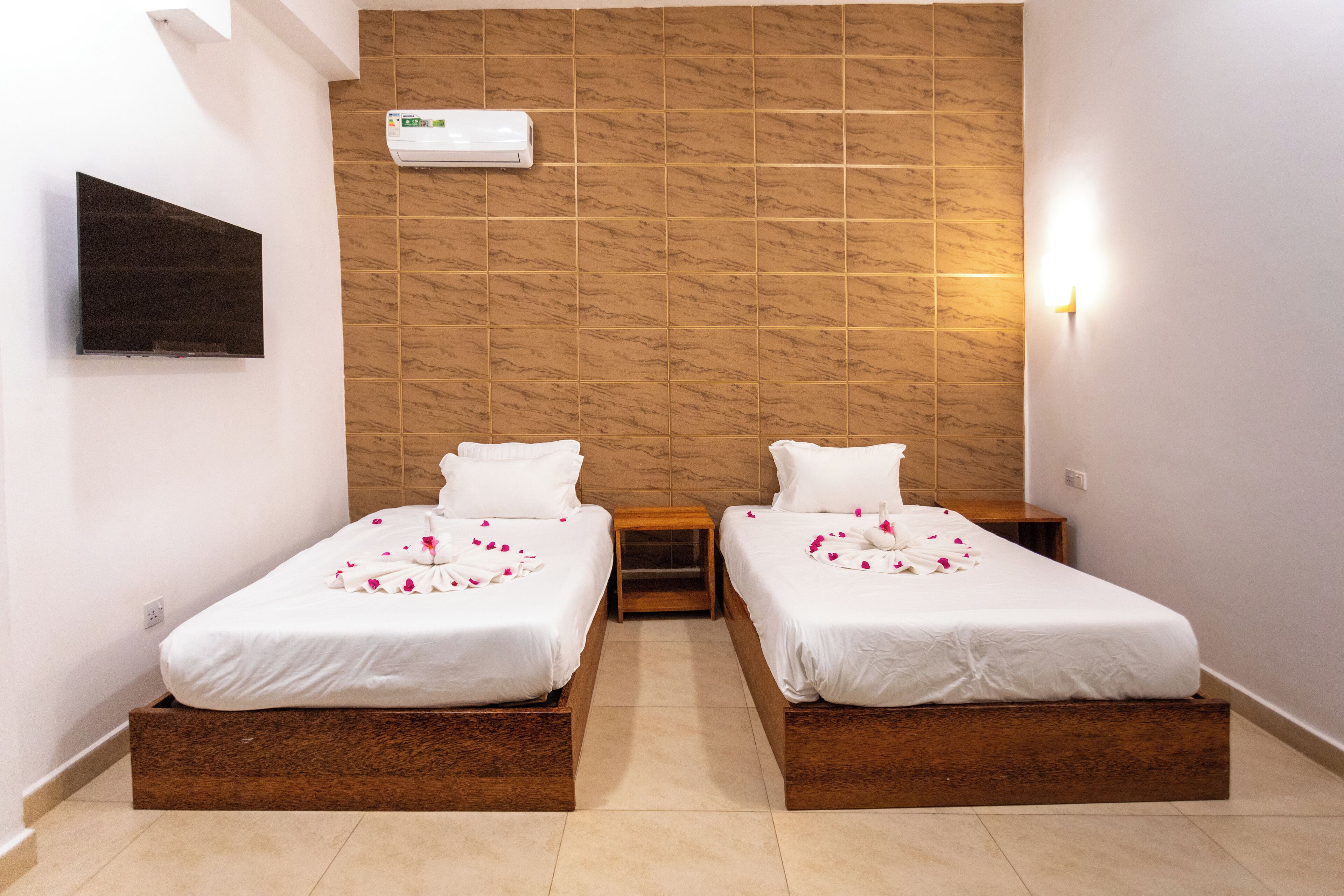 A hotel room with two beds, a TV, a wall-mounted air conditioner, and a small bedside table.