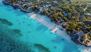 Luchtbeeld van een kustresort met een strand, helder turquoise water en verschillende boten.