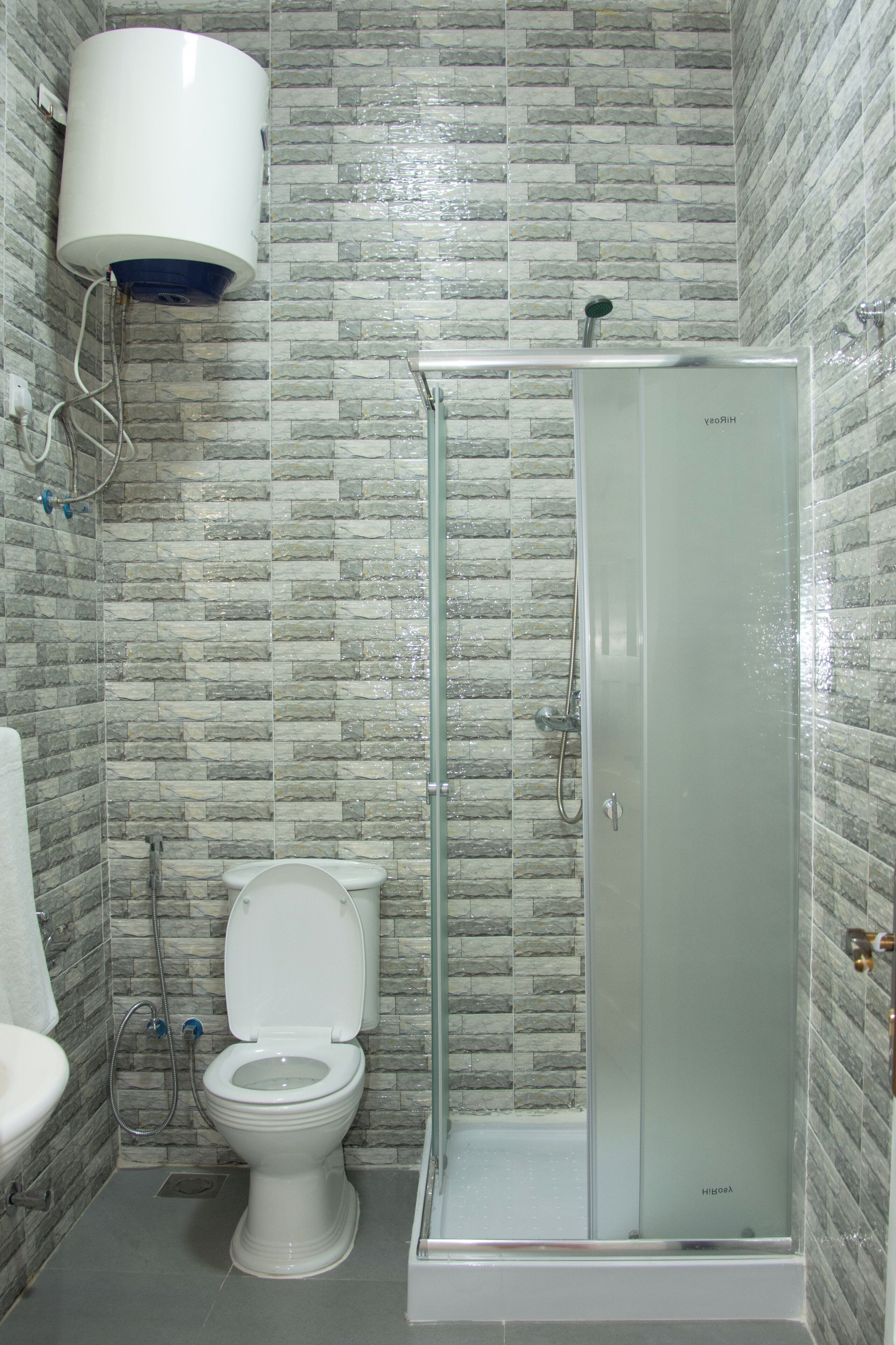 Un baño con inodoro, ducha envuelta en vidrio y calentador de agua instalado en la pared.