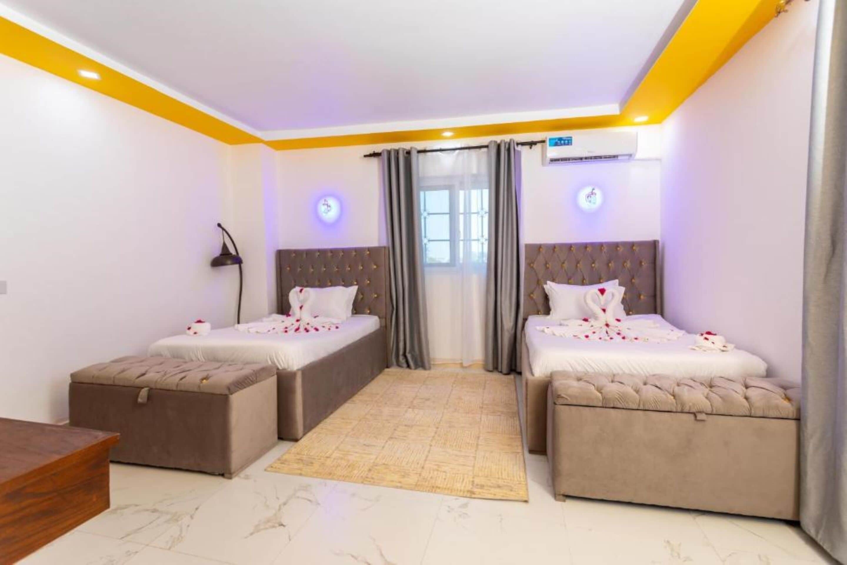 A bedroom with two beds, a bedside table, a lamp, and a window with curtains.