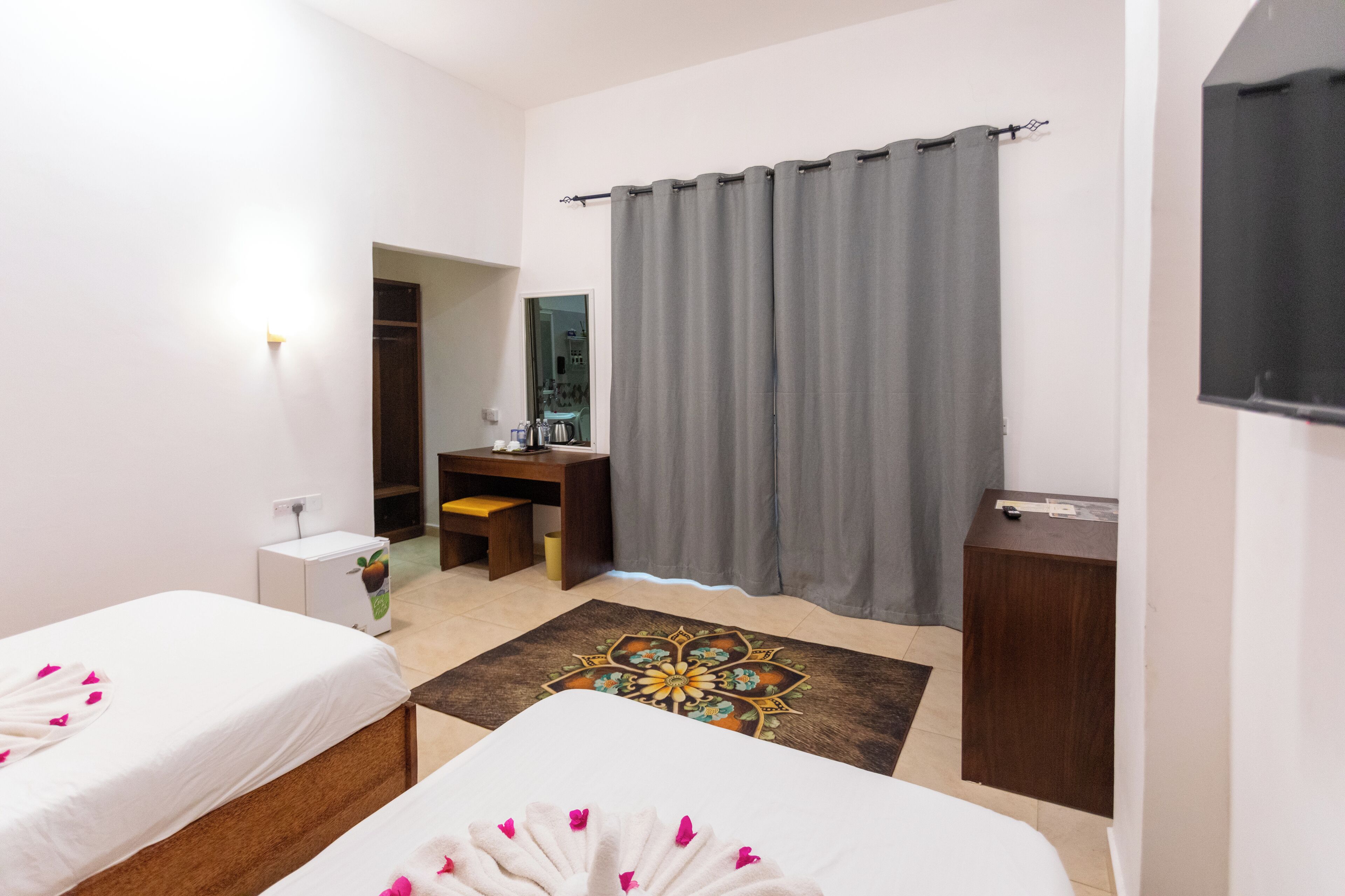 A hotel room with two beds, a desk, a wardrobe, and a television.