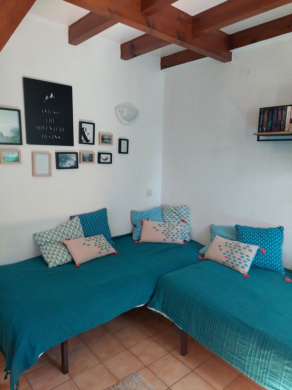 Una habitación con dos camas, una pared con cuadros, una lámpara en el techo y una estantería.