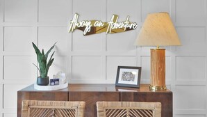 A reception desk with a sign that reads "Always an Adventure," a lamp, a framed picture, and a potted plant. - Lakefront Getaway ☀️ Quiet Canal - Park Your Boat 🚤 4 Bed Townhouse by EverSan Cooper Getaways (Montgomery)