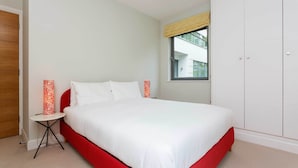 A bedroom with a bed, a small table, a wardrobe, and a window with a view of a building. - Abstract Perspective, by Veeve (London)