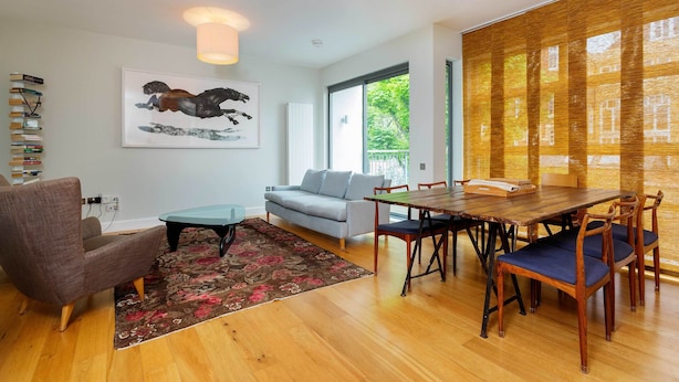 A modern living room with a wooden dining table, blue upholstered chairs, a grey sofa, and a large window with a view of greenery. - Abstract Perspective, by Veeve (London)