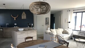A modern living space with a wooden dining table, a sofa, and a kitchen area with a black wall and a hanging light fixture. - Vacation home with jacuzzi 5 minutes from the beach (LE BOIS PLAGE EN RE)