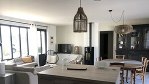A modern kitchen with a central island, a dining area with wooden chairs, and a large window providing natural light. - Vacation home with jacuzzi 5 minutes from the beach (LE BOIS PLAGE EN RE)