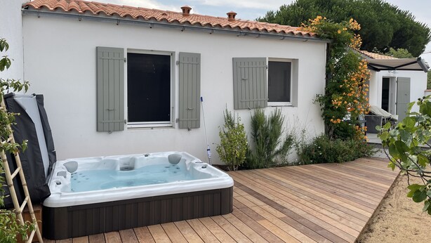 A spa area with a hot tub, wooden deck, and a white building with green shutters. - Vacation home with jacuzzi 5 minutes from the beach (LE BOIS PLAGE EN RE)