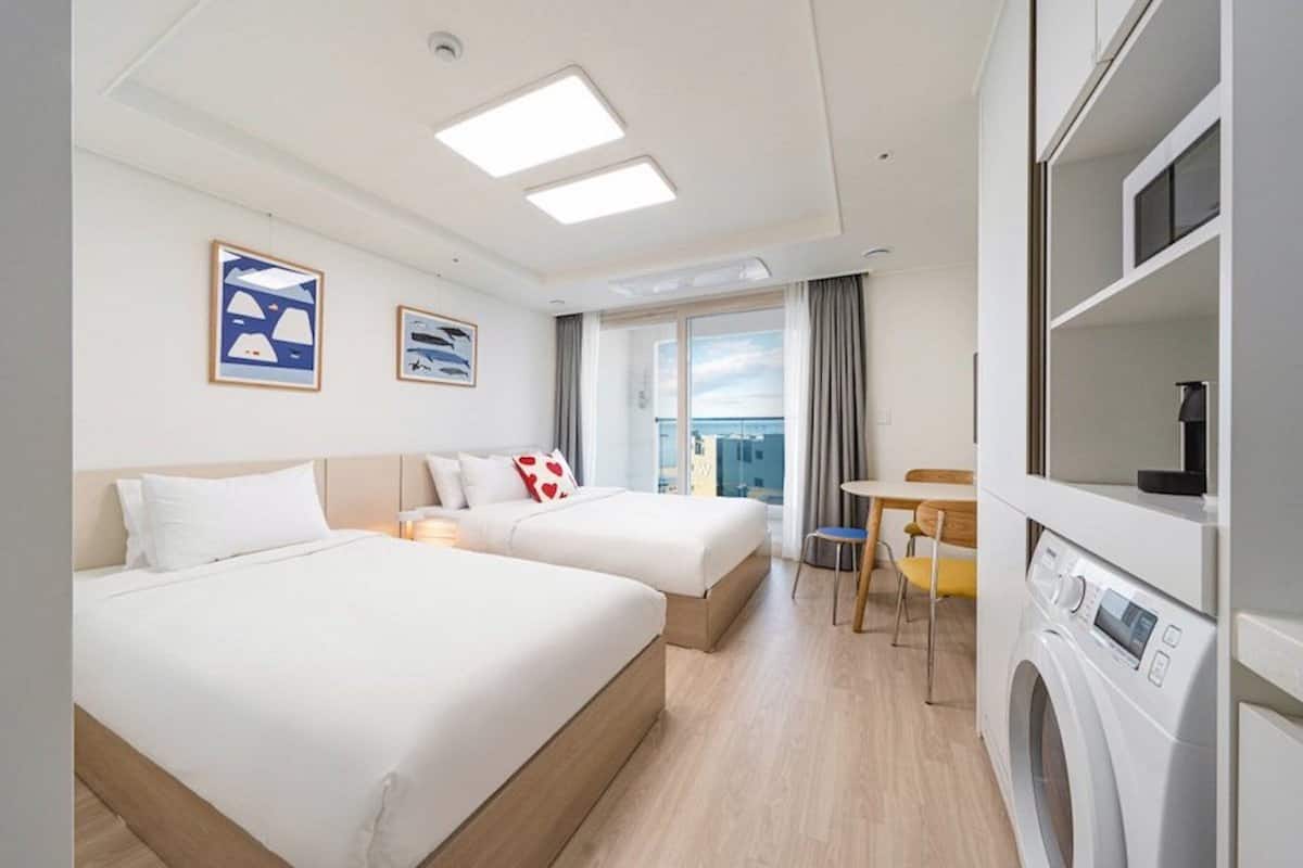 Quarto de hotel com duas camas, área de refeições e máquina de lavar.