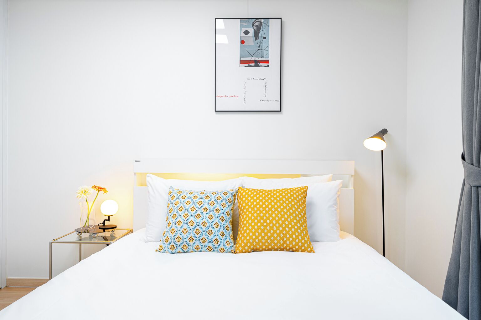 Quarto de hotel bem arrumado com uma cama, uma mesinha de cabeceira com abajur e um quadro na parede.