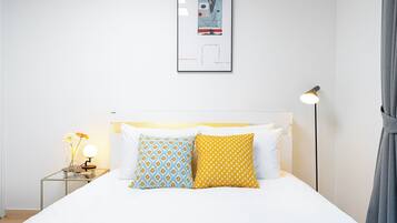 Quarto de hotel bem arrumado com uma cama, uma mesinha de cabeceira com abajur e um quadro na parede.