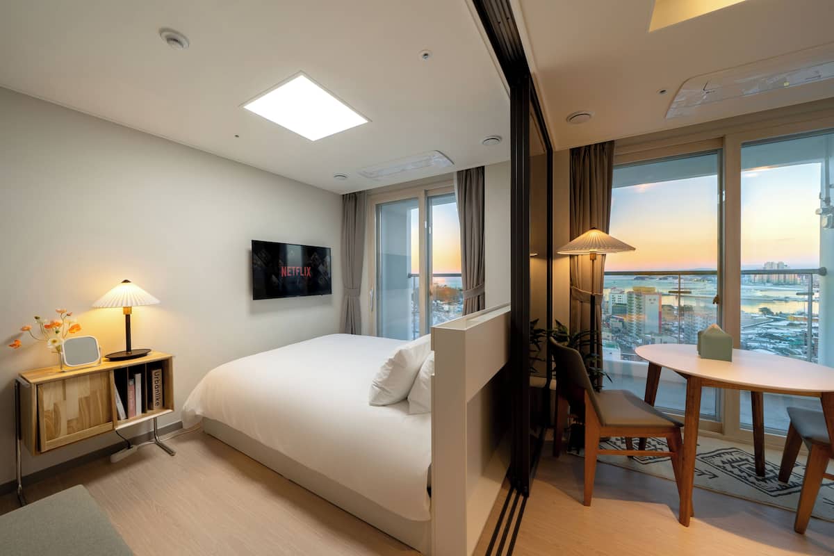 Quarto de hotel com uma cama, uma escrivaninha com abajur, uma televisão e vista para a cidade.