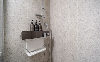 Zona de ducha con un estante integrado que contiene tres botellas de productos para el cabello.