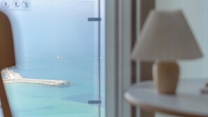 Een kamer met uitzicht op zee door een raam, een lamp op een bijzettafeltje en een deur met een deurklink.