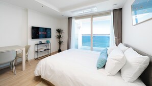 Een moderne hotelkamer met een groot bed, een bureau, een televisie en een balkon met uitzicht op zee.