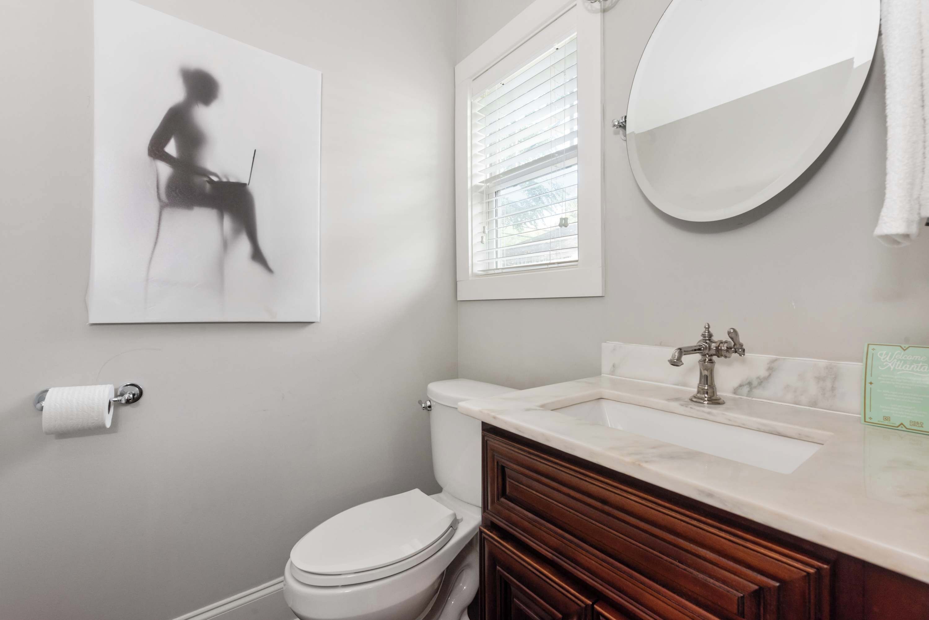 Une salle de bain équipée de toilettes, d’un lavabo, d’un miroir et d’un tableau encadré accroché au mur.