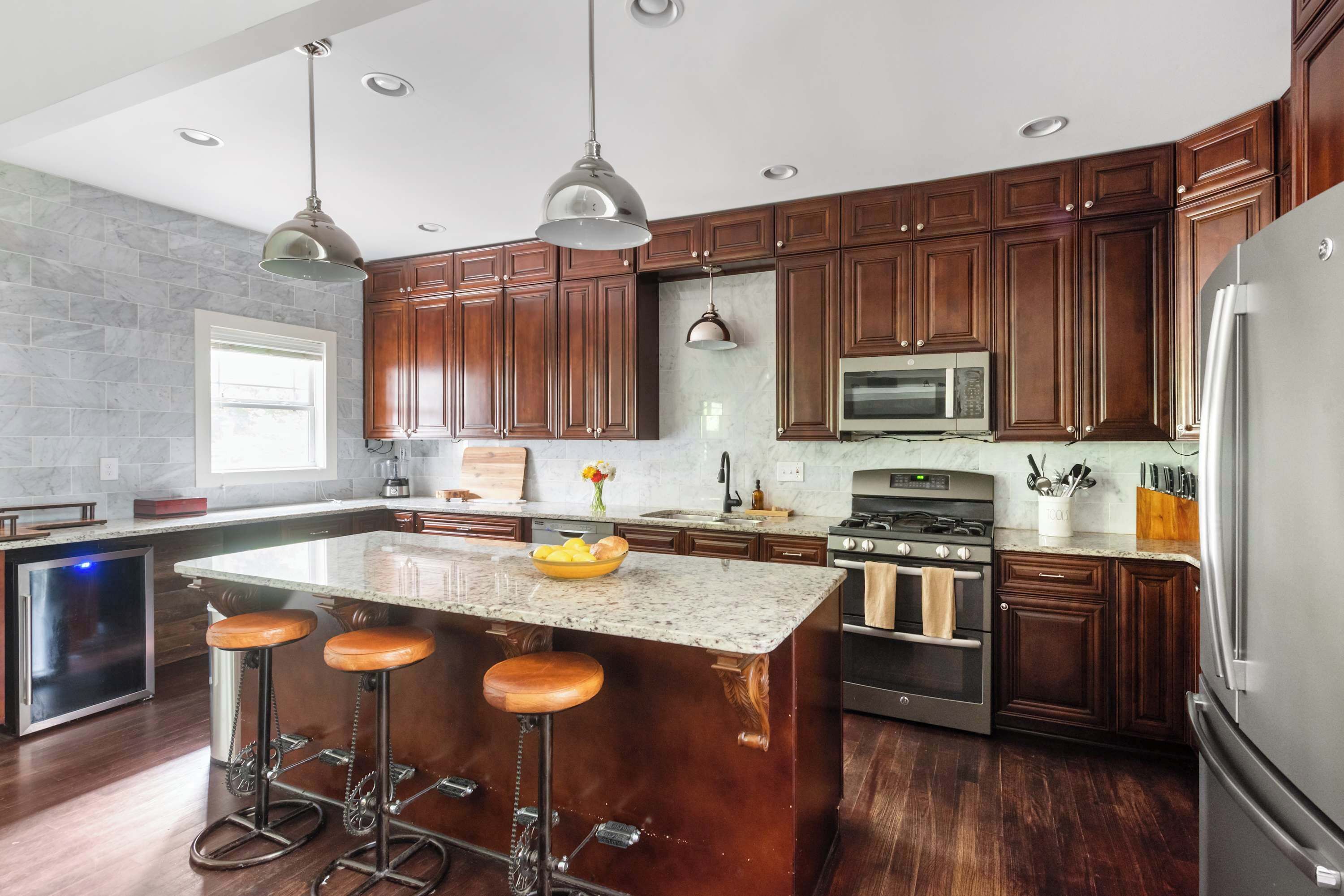 A modern kitchen with dark wooden cabinets, stainless steel appliances, and a central island with stools.
