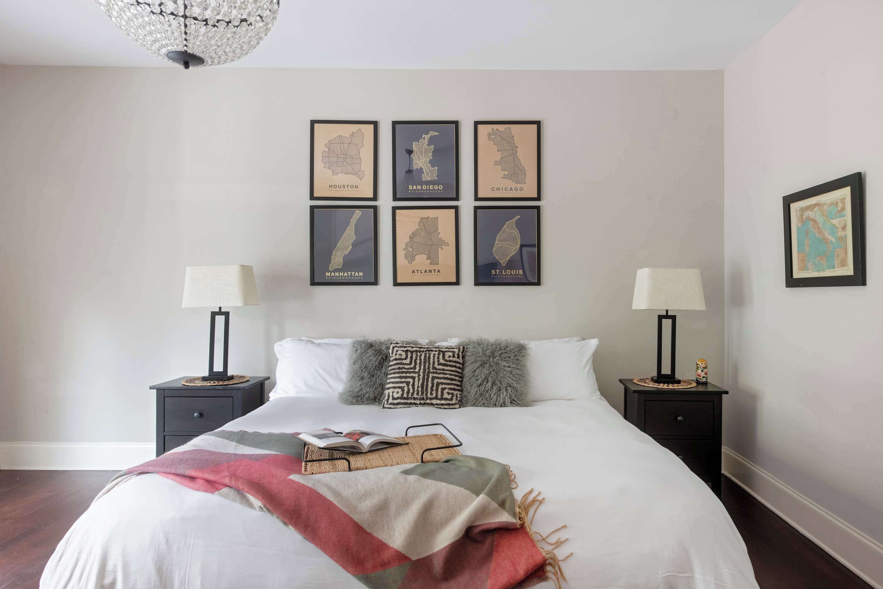 A bedroom with a bed, two nightstands, a chandelier, and framed maps of cities on the wall.