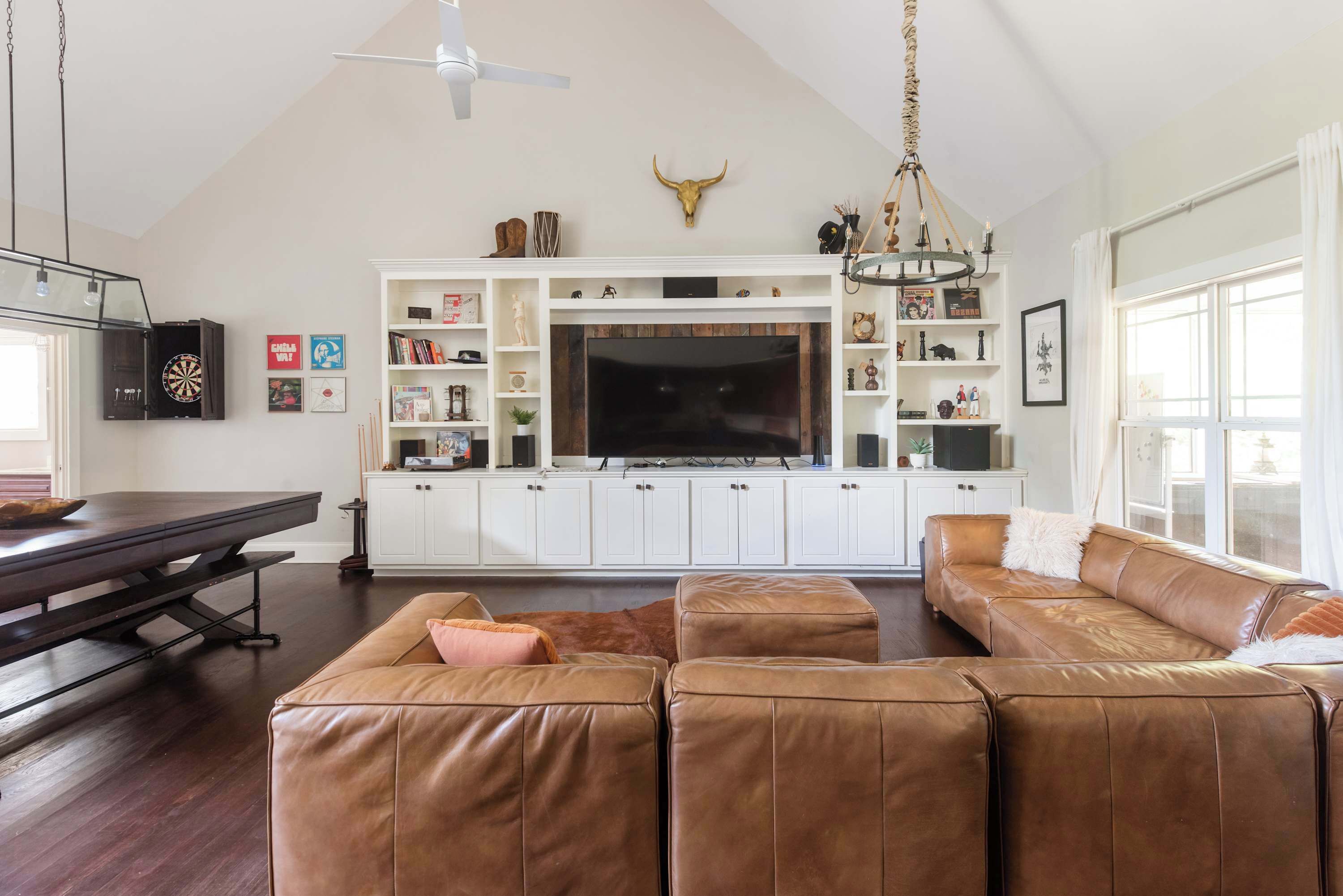 A spacious living room with a large leather sofa, a dining table, and a TV mounted on a white cabinet.