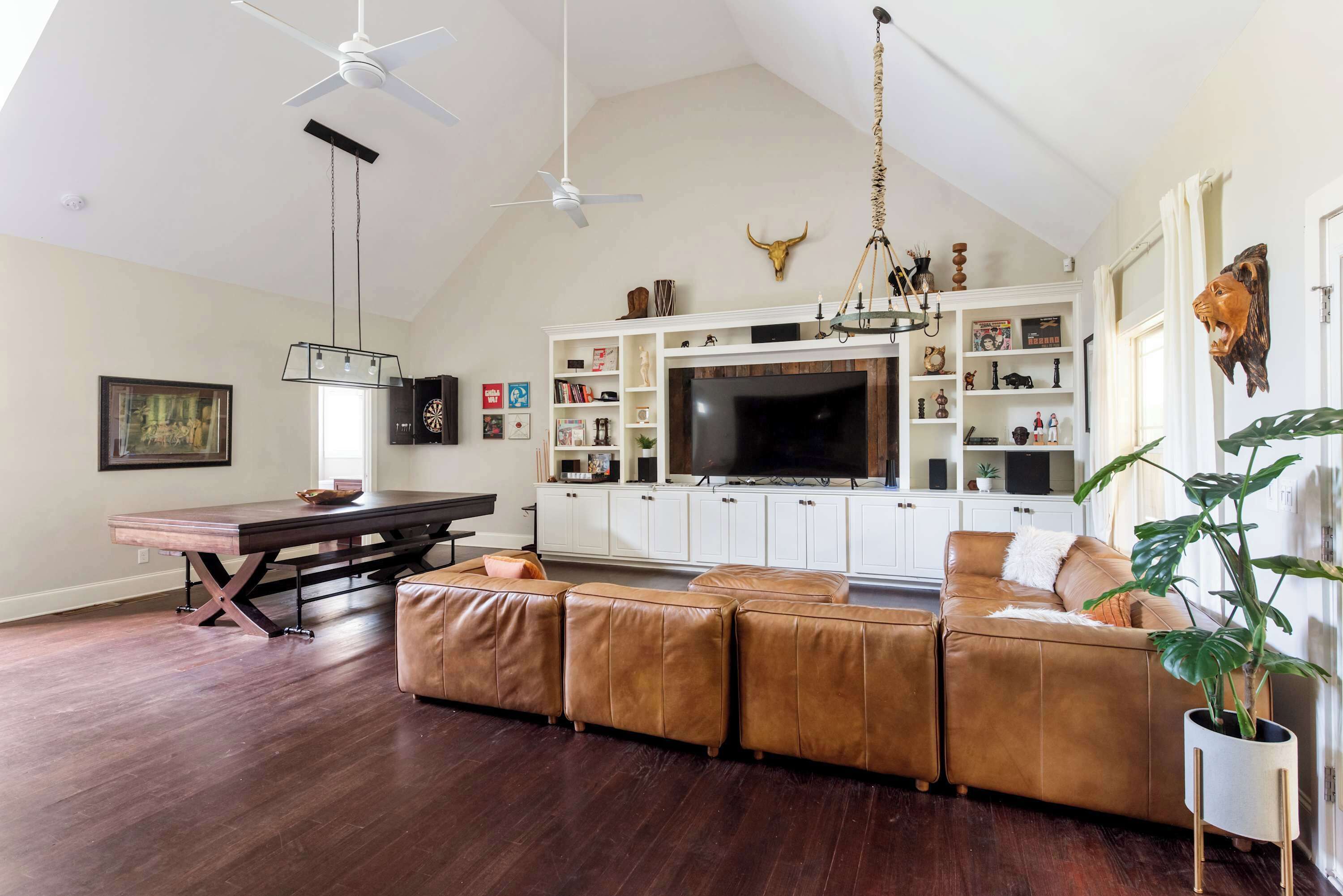 A spacious living room with a large L-shaped sectional sofa, a dining table, and a TV mounted on a white cabinet.