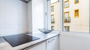 Eine Küche mit Fenster, weißen Fliesen, einer schwarzen Induktionskochplatte und Blick auf ein gelbes Gebäude.