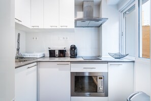 A modern kitchen with white cabinetry, a built-in oven, a coffee maker, and a window.