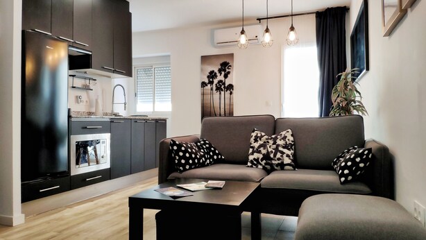 Una sala de estar moderna con un sofá, una mesa de centro y una zona de cocina con armarios y electrodomésticos.