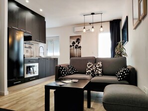 A modern living room with a sofa, coffee table, and kitchen area with cabinets and appliances. - Apartment Estrella de Mar close to the Beach with Terrace, Balcony & Wi-Fi (Vinaròs)