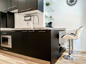 Une cuisine moderne avec des meubles de couleur sombre, un four en acier inoxydable, une machine à café et un tabouret de bar.
