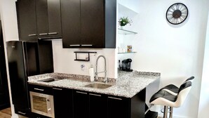 Cocina moderna con armarios oscuros, encimera de granito, horno integrado, pileta de acero inoxidable y cafetera.